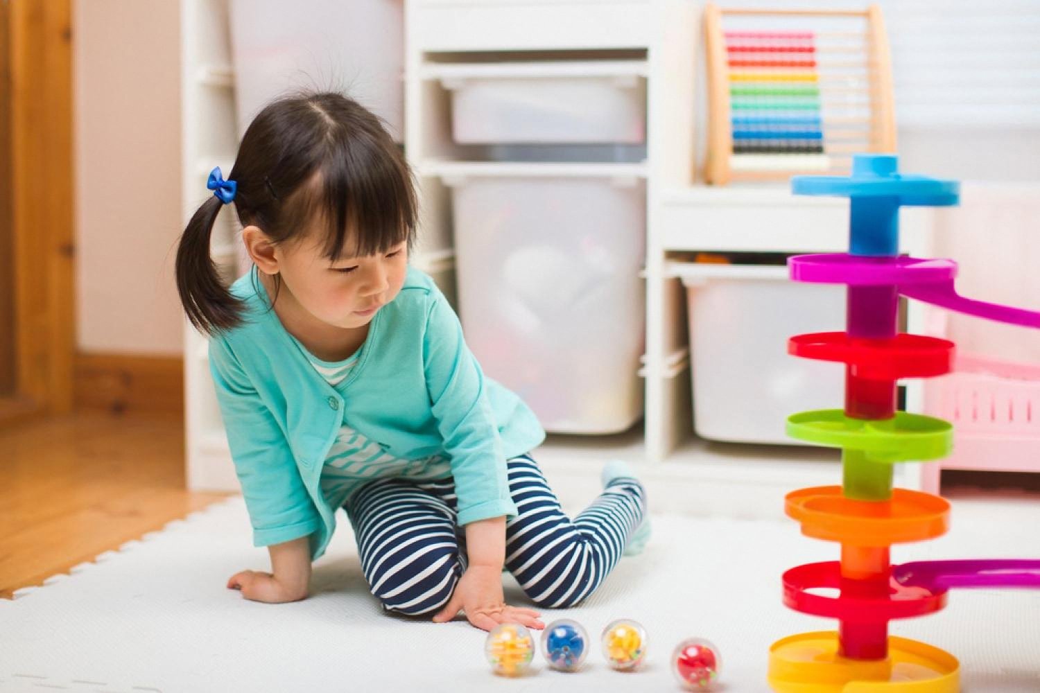 Young girl focused on a colourful marble run tower toy at home