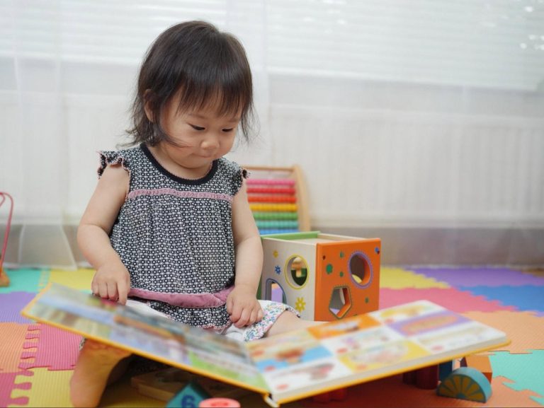 Toddler in Dubai playing with a shape sorter cube and a picture book on a play mat