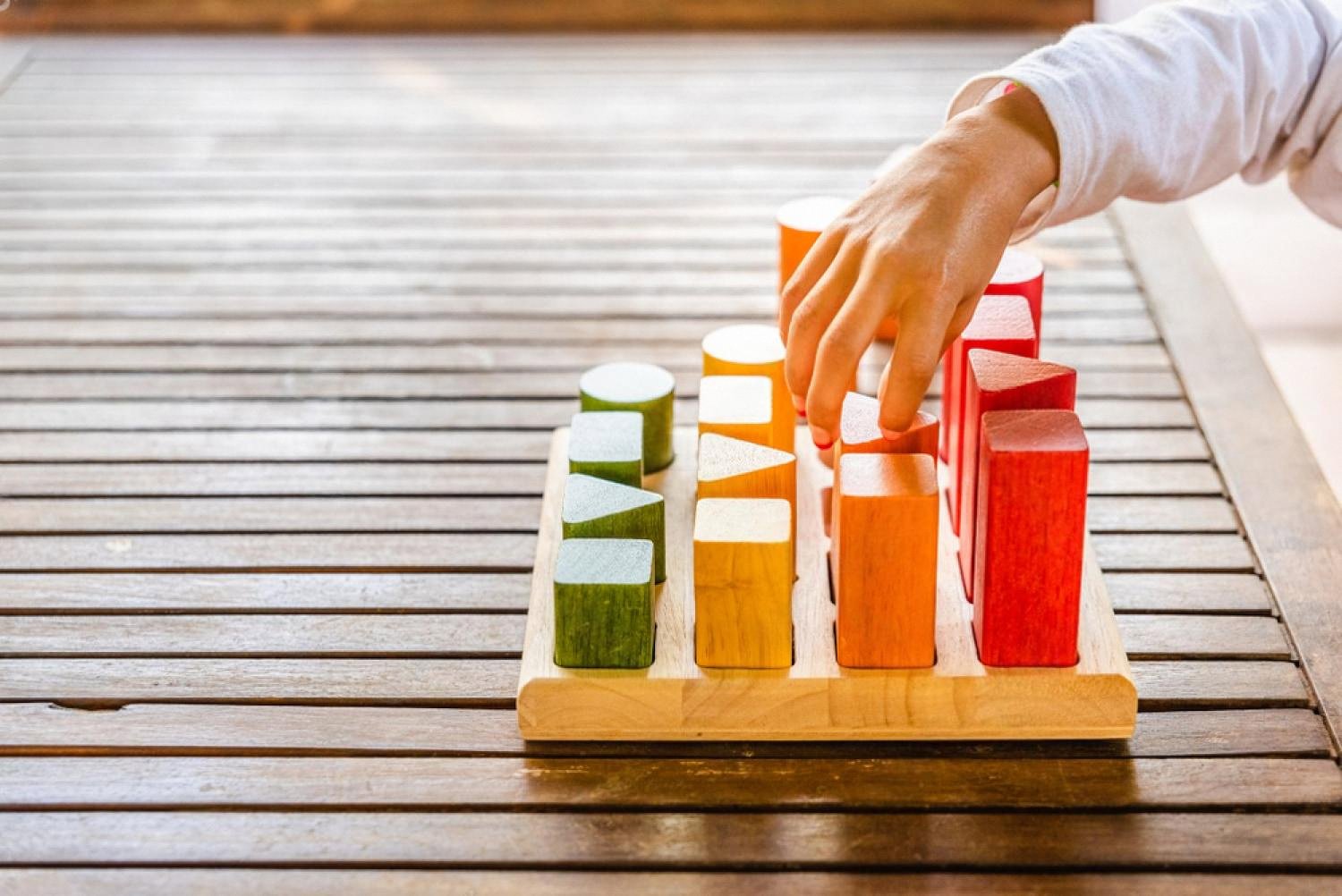 Child's hand sorting coloured wooden blocks by shape and size on a sorting board